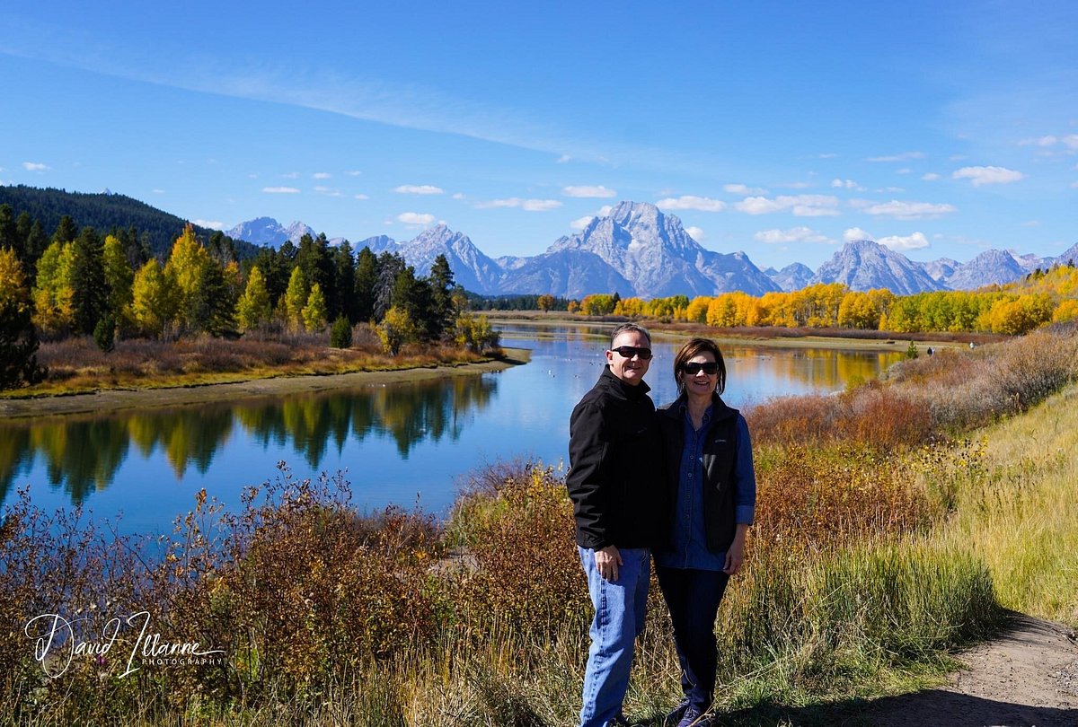 Couple posing for photo in front of reflective river mirroring Teton mountains